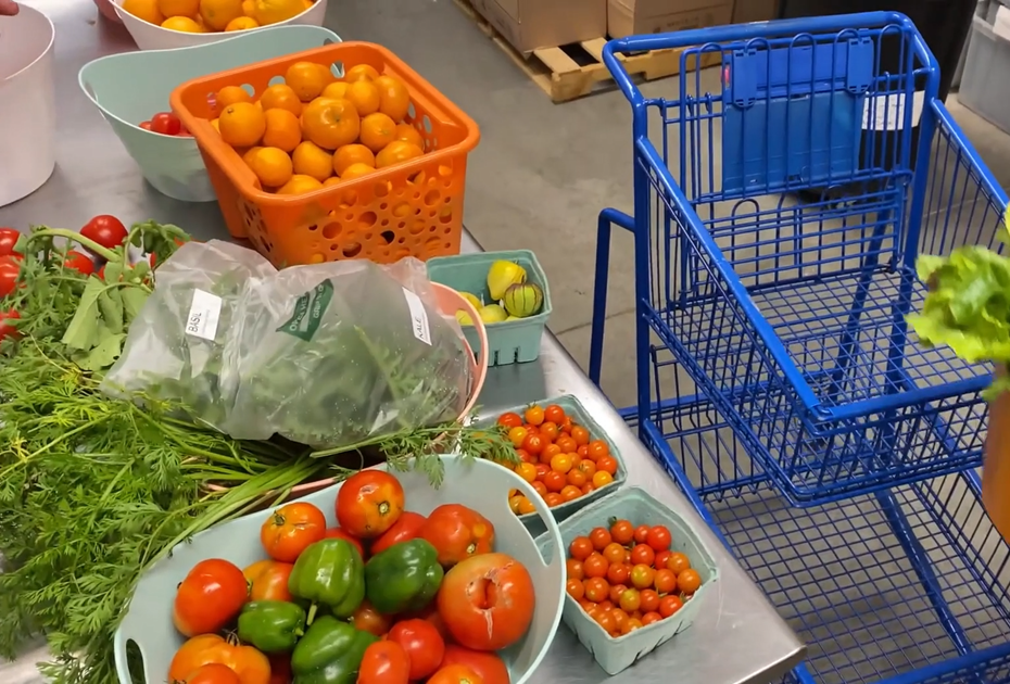 Various produce on a counter, with a blue shopping cart alongside and more produce in the background.